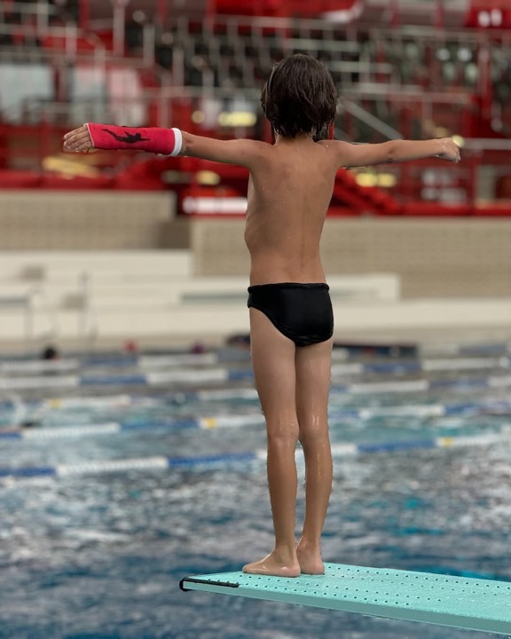 Bub mit rotem Schwimmgips am Sprungbrett im Schwimmbad