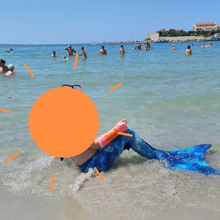 Kind mit Schwimmgips und Meerjungfrauen-Flosse am Strand